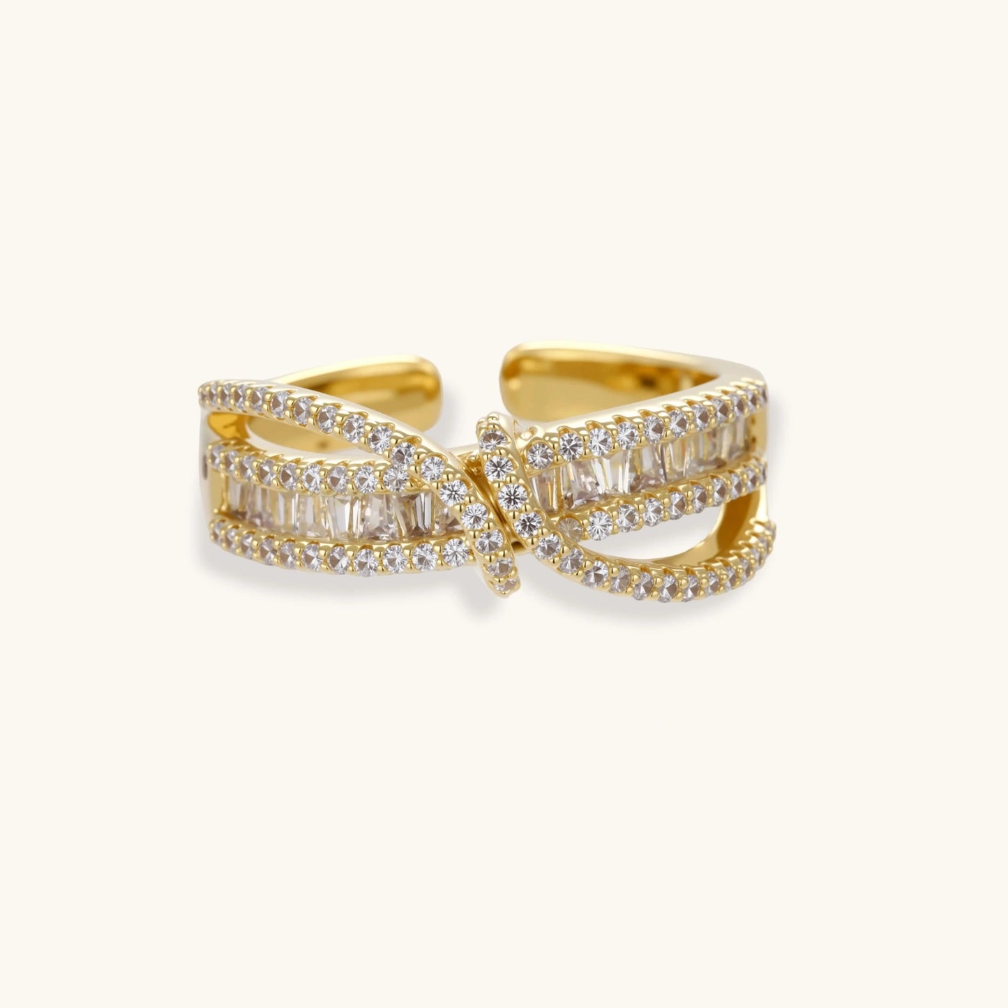 Close-up of gold-plated adjustable ring with crossing bands and sparkling zirconia stones on white background.