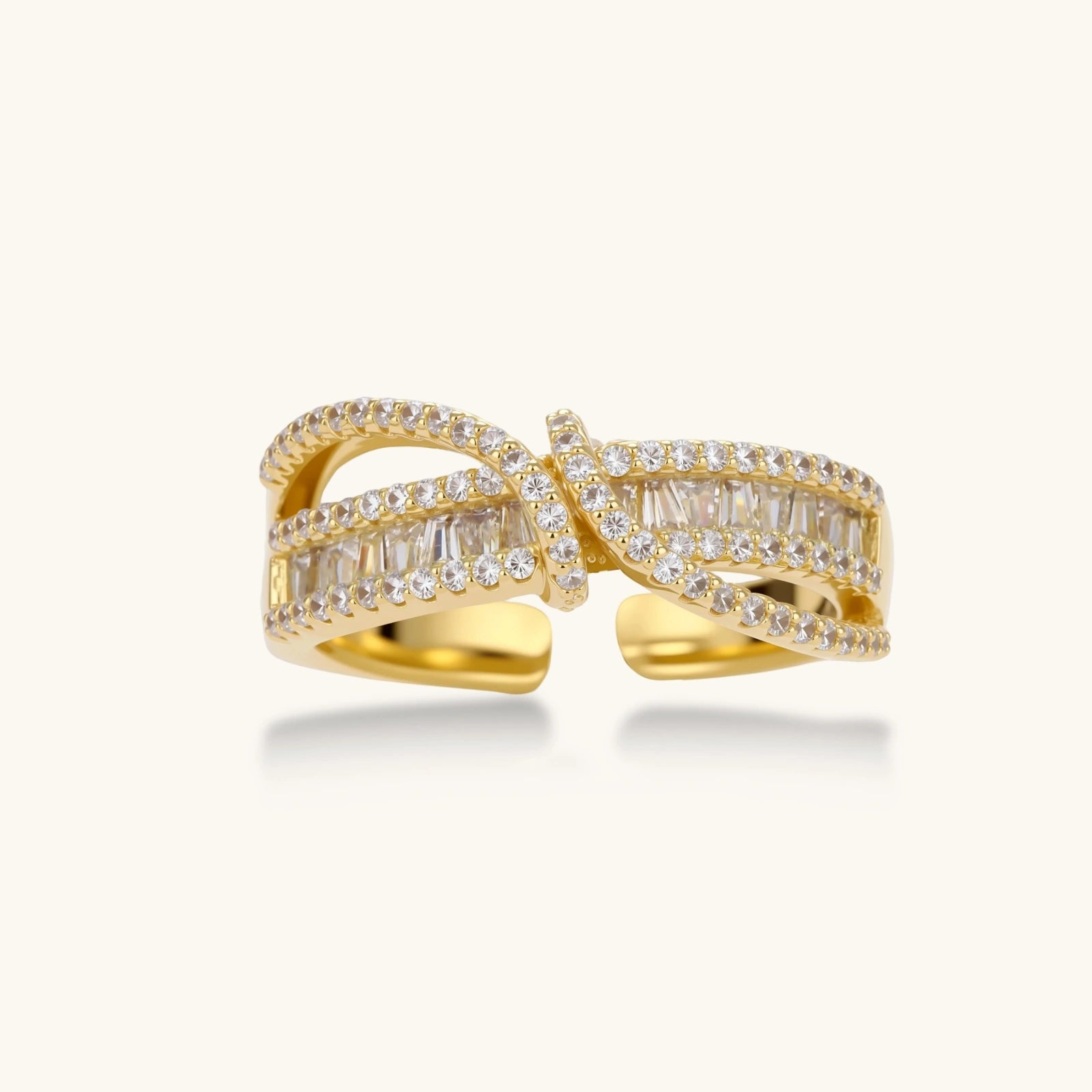 Close-up of gold-plated adjustable ring with crossing bands and sparkling zirconia stones on white background.