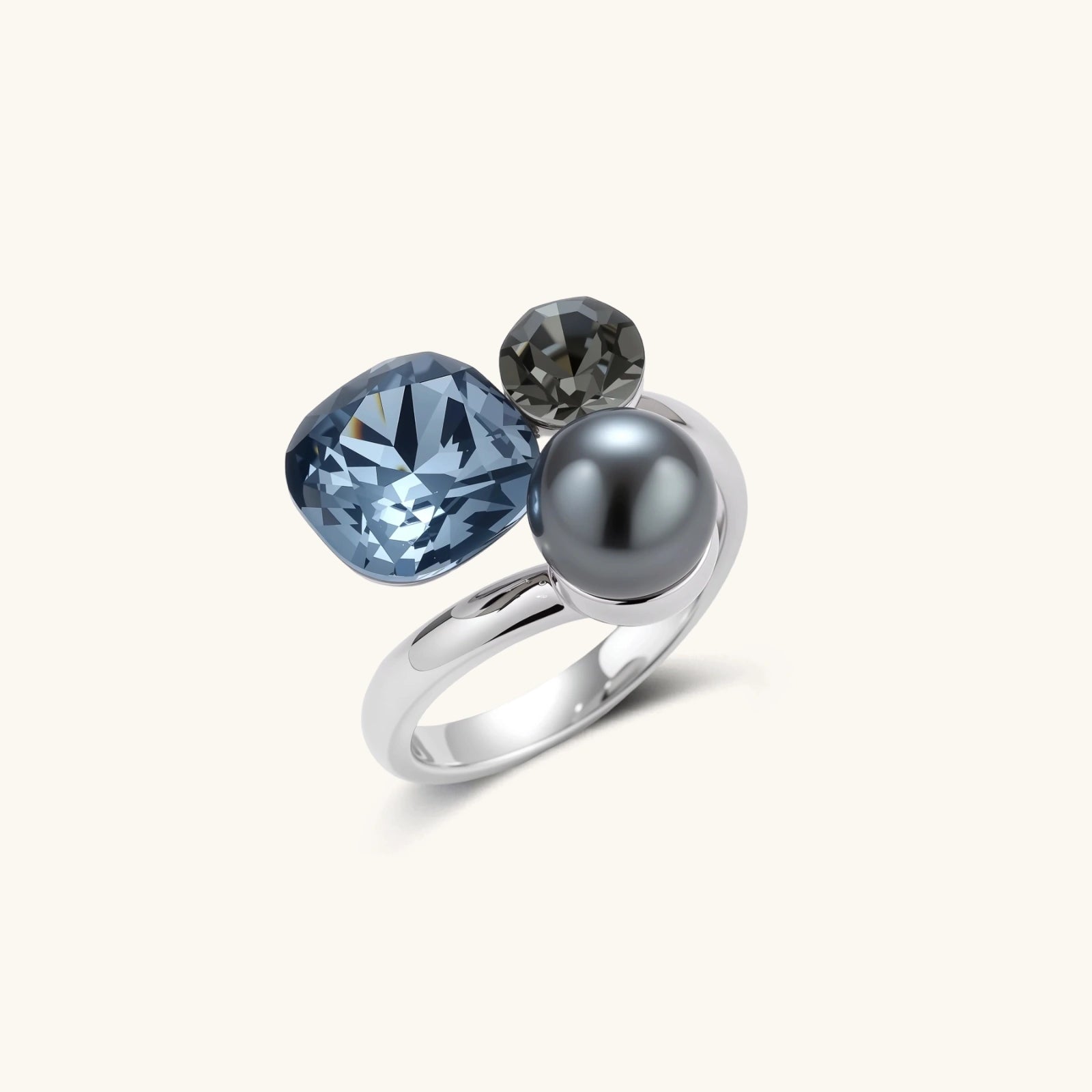 Adjustable ring with blue cushion-cut zirconia, gray pearl, and dark crystal on platinum-plated copper band against beige background.