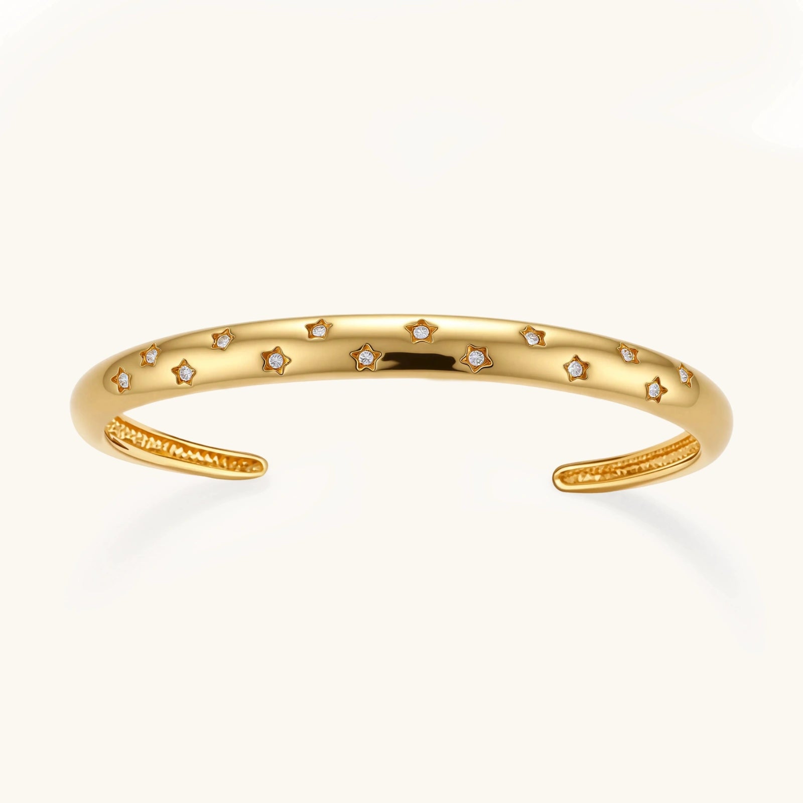 Polished 18K gold plated cuff bracelet with cubic zirconia set in star motifs on a cream background.