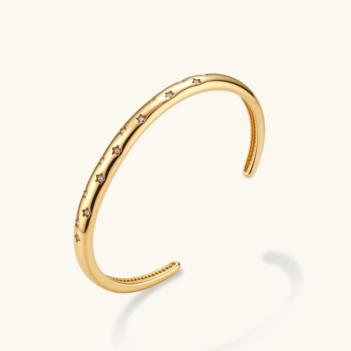 Polished 18K gold plated cuff bracelet with cubic zirconia set in star motifs on a cream background.